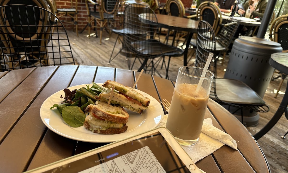 A pressed sandwich with pesto and a side salad next to an iced latte on the patio at Cafe Loft