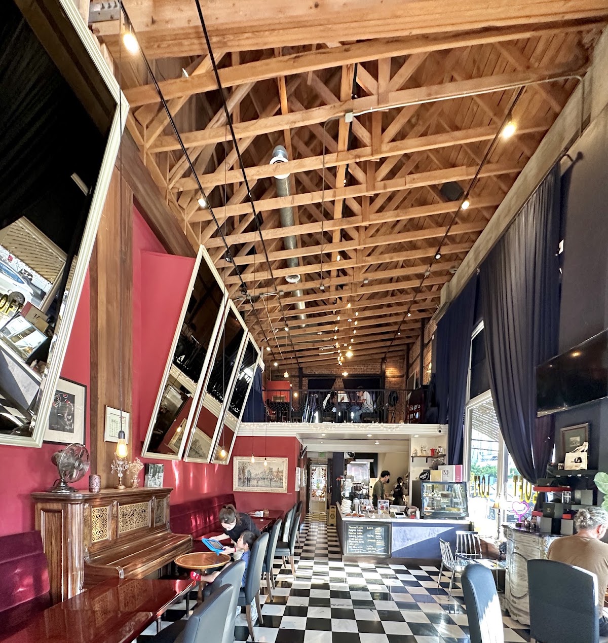 The interior of Cafe Loft, with exposed timber roof trusses, crimson walls, gilt mirrors and a black and white checkerboard floor