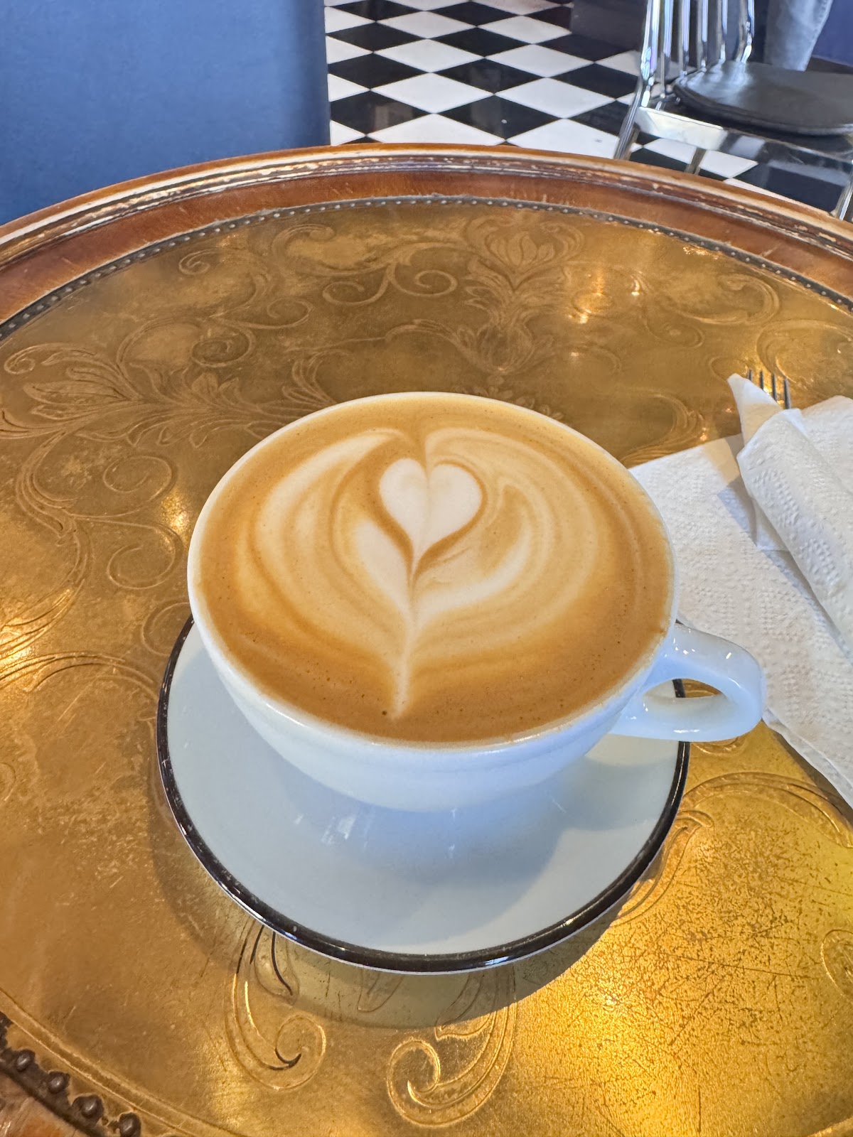 A latte with heart shaped latte art in a white cup on an engraved gold tray