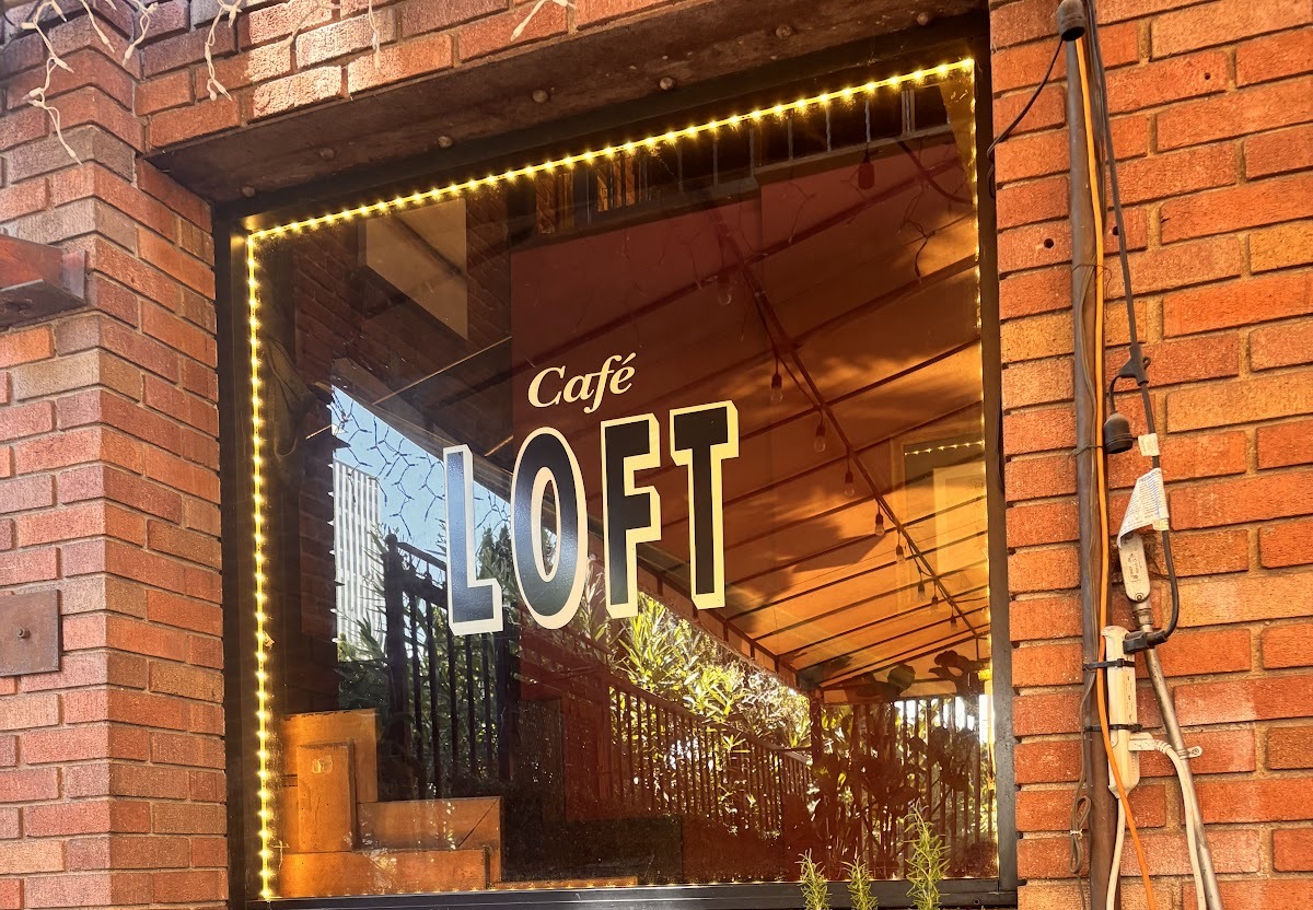The Cafe LOFT window decal on the red brick exterior, framed by warm fairy lights