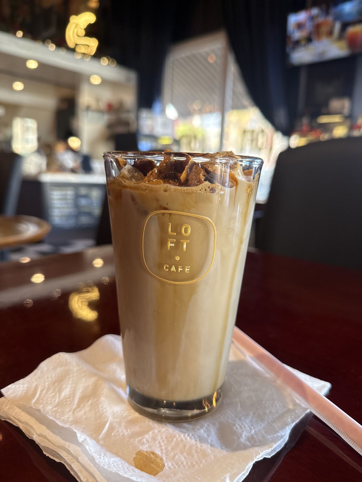 An iced latte in a Cafe Loft branded glass, with the gold LOFT CAFE mark on the side