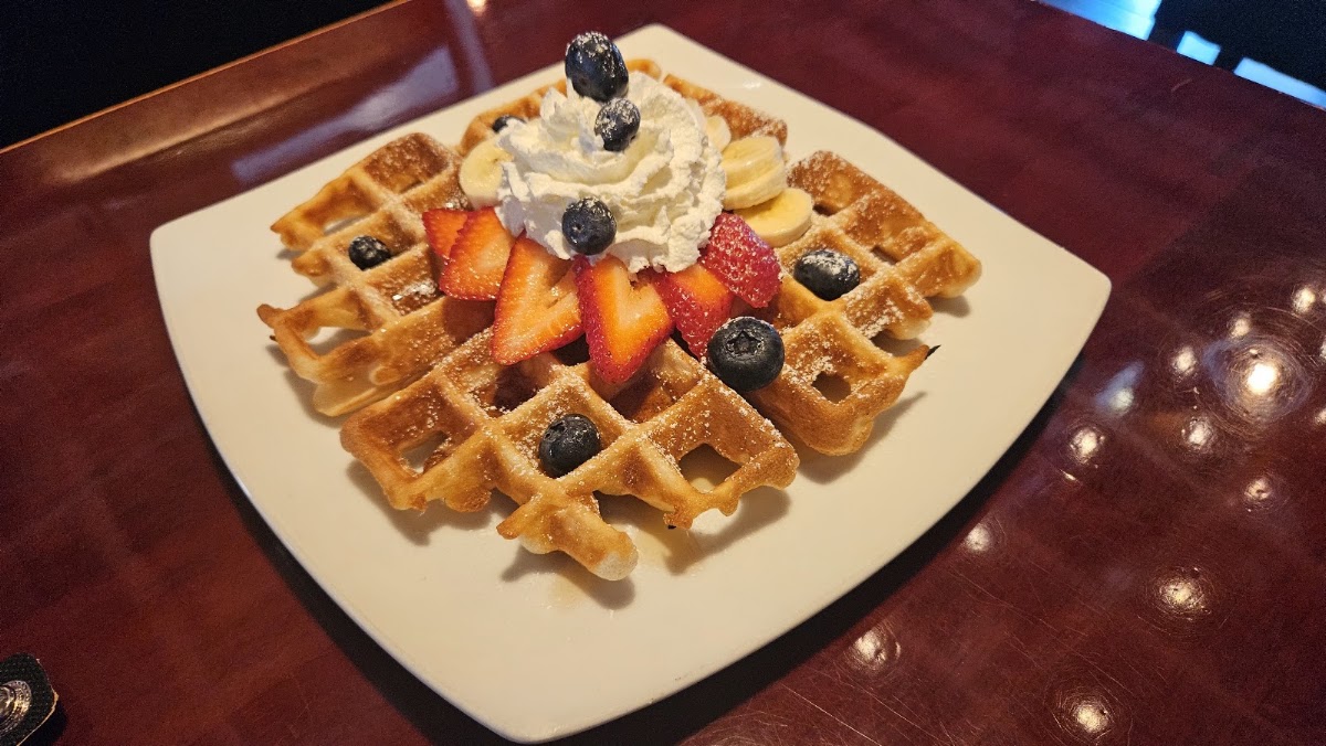 A Belgian waffle with strawberries, blueberries, banana and whipped cream