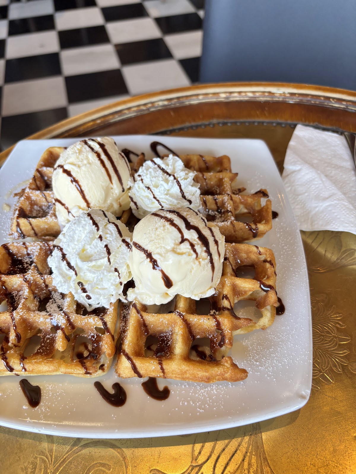 Belgian waffles topped with four scoops of ice cream and chocolate sauce on a gold tray